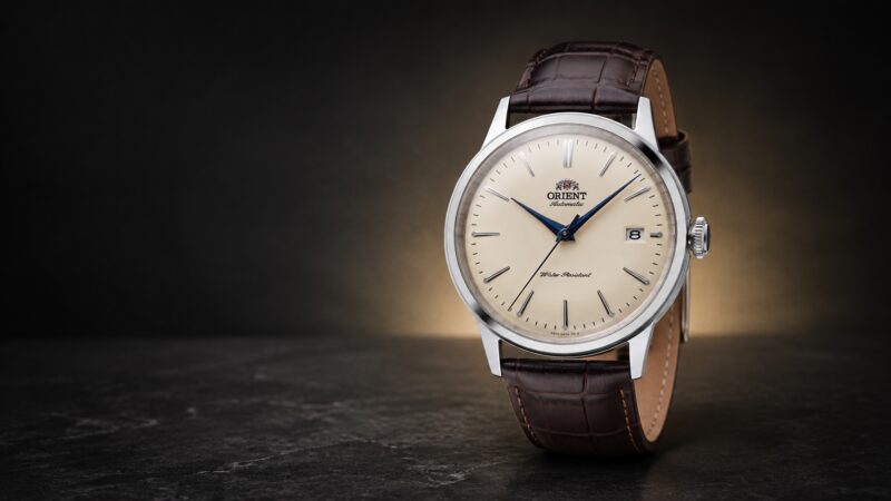 Cream-dial Orient Bambino 38 RA-AC0M04Y with blue hands and brown leather strap in a dark studio setting.
